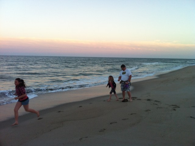 man and children playing on beach at sunset
